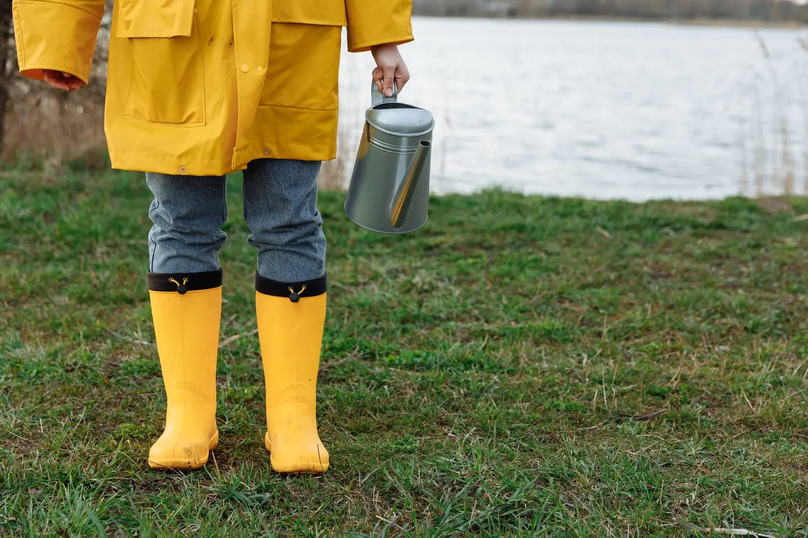 A person in yellow rubber boots carrying a metal pail across grass