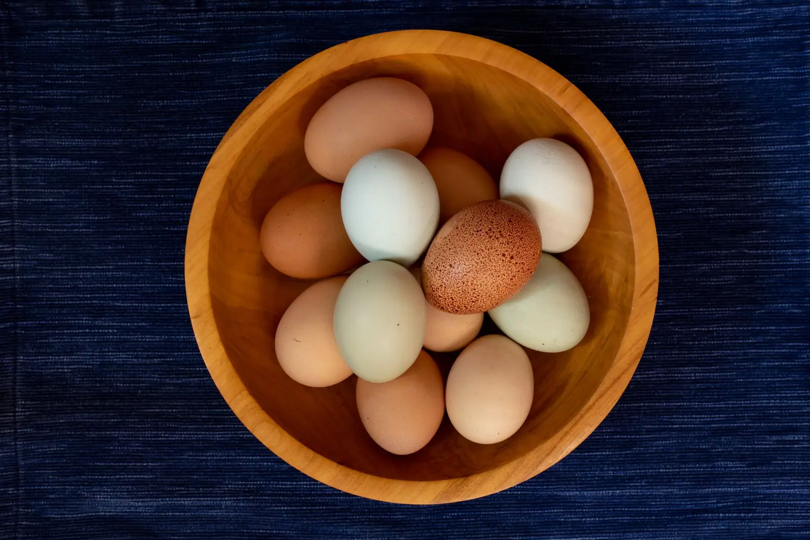A wooden bowl of brown, cream and pale green eggs