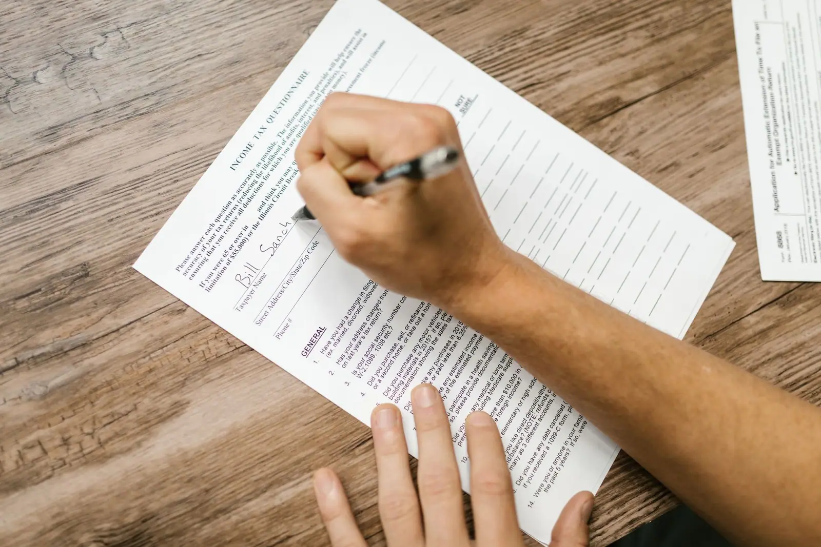 A person filling in a printed form by hand at a wooden table