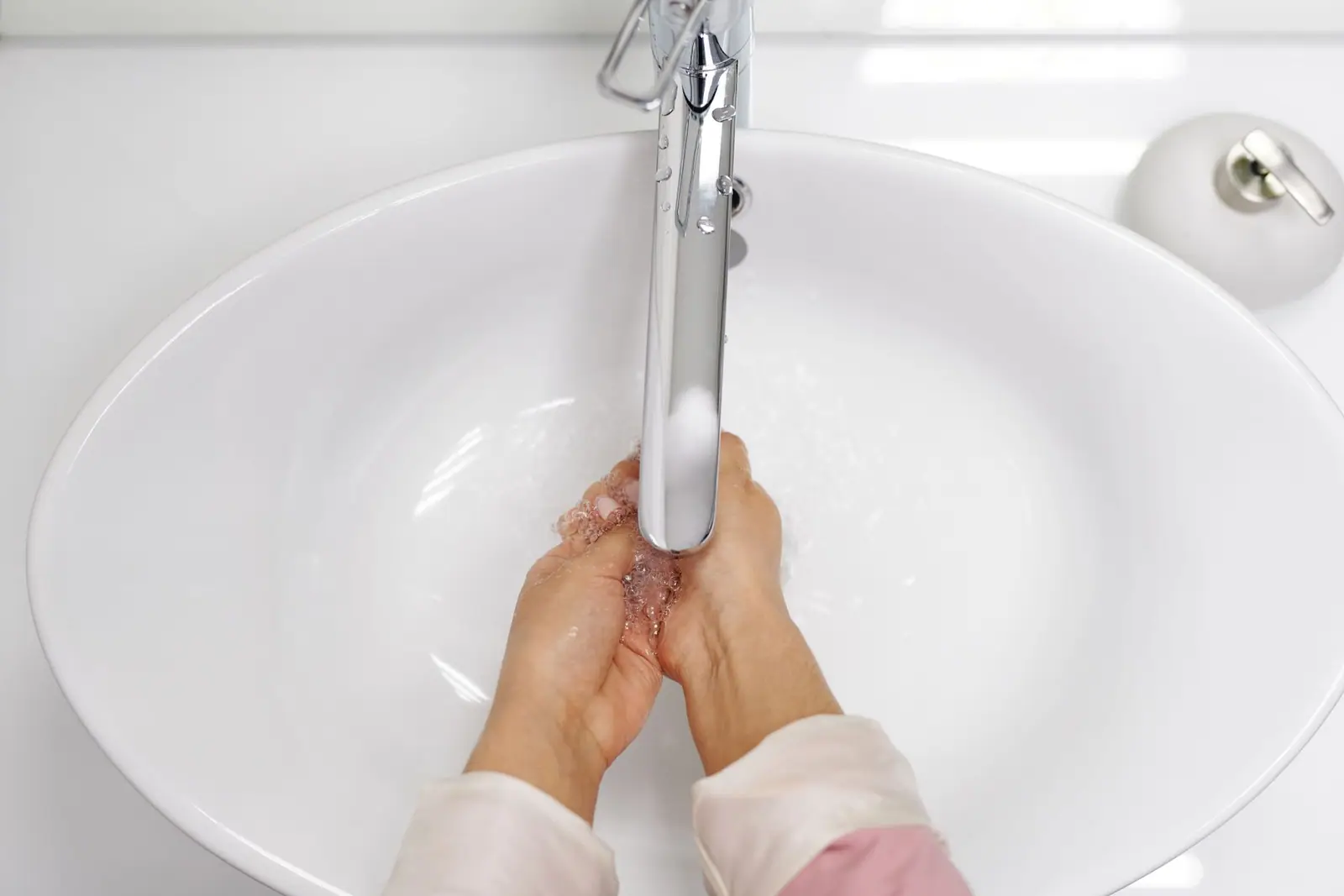 Hands being washed under a running tap over a white sink
